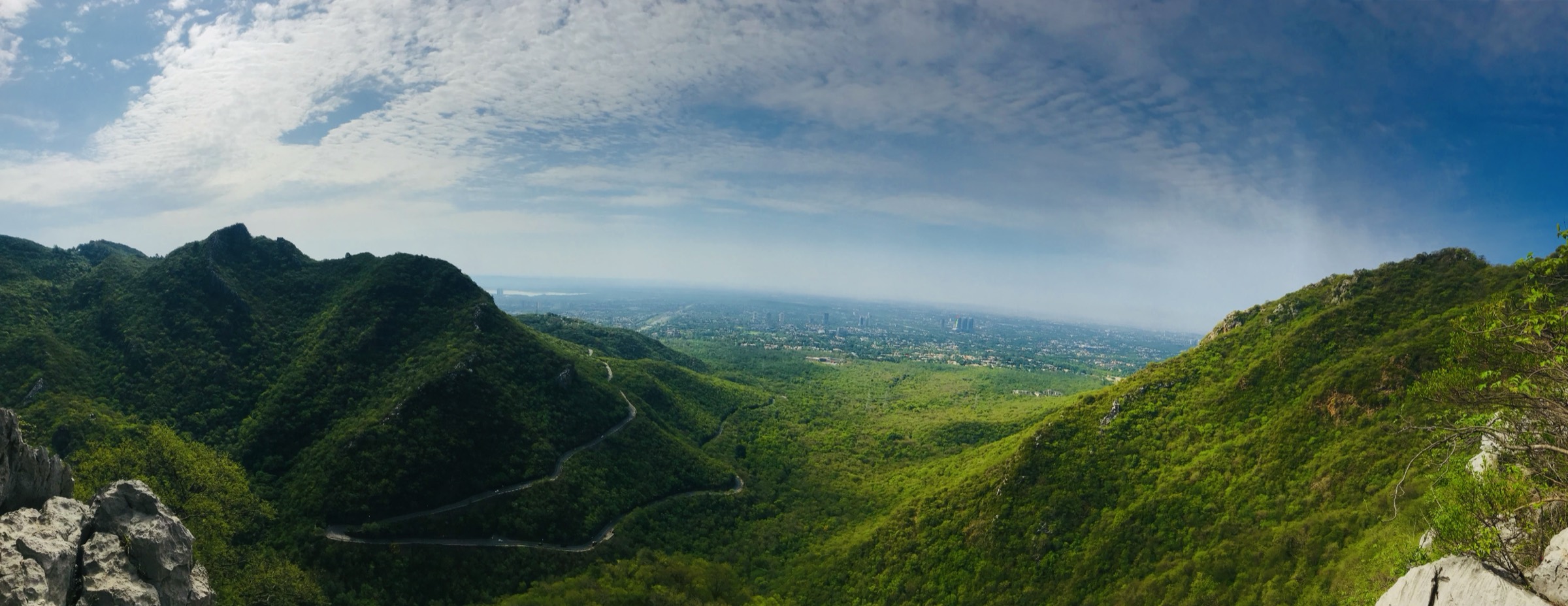 Panorama from the Margalla Hills: green ridges, a winding road and Islamabad on the plain beyond